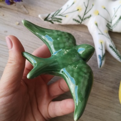 Figura cerâmica de pássaro esmaltada verde sendo segurada por mão