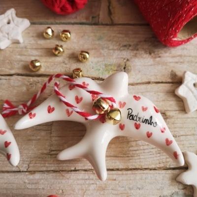 Figurinha de golfinho branco decorado com corações vermelhos e guizos, com fundo de mesa de madeira e fios de lã vermelha