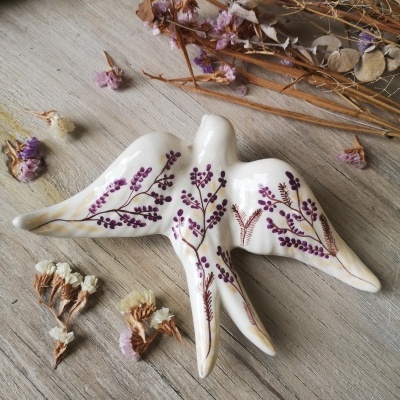 Figura decorativa em cerâmica branca com pintura floral roxa, sobre madeira clara e flores secas