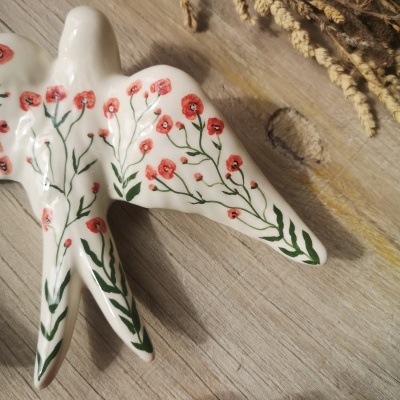 Escultura cerâmica pássaro branca com flores vermelhas e verdes sobre madeira clara