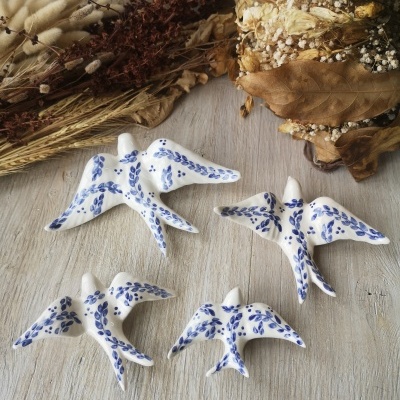 Figuras cerâmicas de pássaros brancas com padrões azuis e plantas secas ao fundo