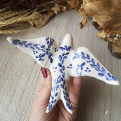 Escultura de cerâmica branca com detalhes azuis em forma de pássaro com asas abertas