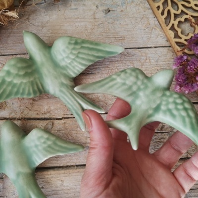 Figuras decorativas de pássaros verdes com textura em madeira rústica e flores secas lilás