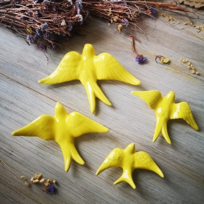 Quatro pássaros decorativos amarelos em cerâmica sobre madeira com ramos secos ao fundo