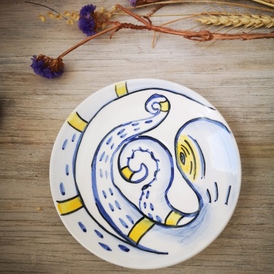 Prato de cerâmica com padrão azul e amarelo sobre mesa de madeira com flores secas