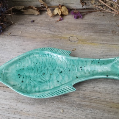 Prato de cerâmica verde em forma de peixe sobre madeira clara