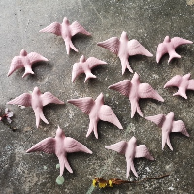 Doze estatuetas rosa de pássaros sobre superfície cinza com flores secas