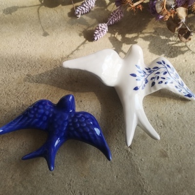 Dois pássaros decorativos em cerâmica, um azul e outro branco com detalhes azuis