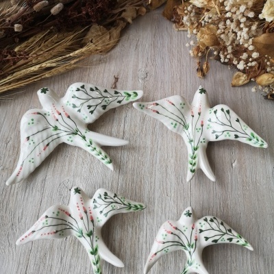 Esculturas decorativas de pássaros brancos com pintura floral em verde e vermelho sobre madeira clara