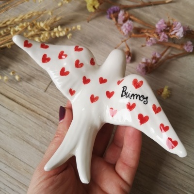 Pássaro decorativo em cerâmica branca com corações vermelhos e texto 'Bunos'