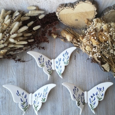 Borboletas decorativas de cerâmica com flores azuis sobre madeira clara com ramos secos ao redor
