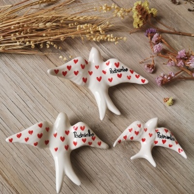 Figuras de pássaros brancos decorados com corações vermelhos e a palavra 'Padrinho' sobre madeira clara