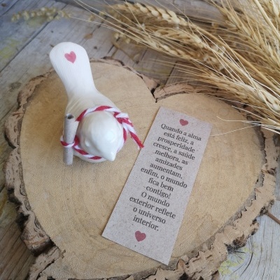 Figura de cerâmica branca com coração vermelho sobre base de madeira em formato de coração com cartão de mensagem e espigas secas