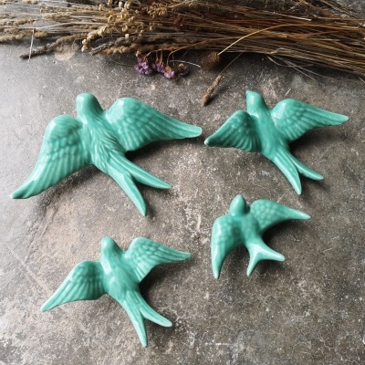 Estatuetas de pássaros em cerâmica verde turquesa sobre superfície cinza com ramos secos ao fundo