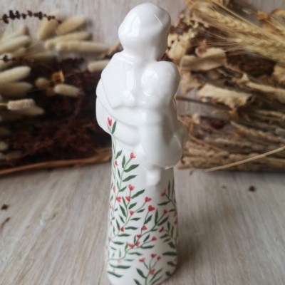 estátua de cerâmica branca com detalhes florais verdes e vermelhos em fundo de flores secas
