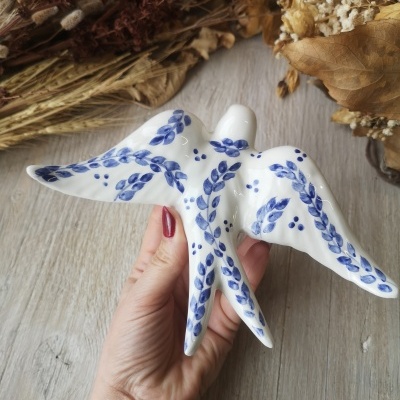 Escultura em cerâmica branca com padrão azul segurada por mão