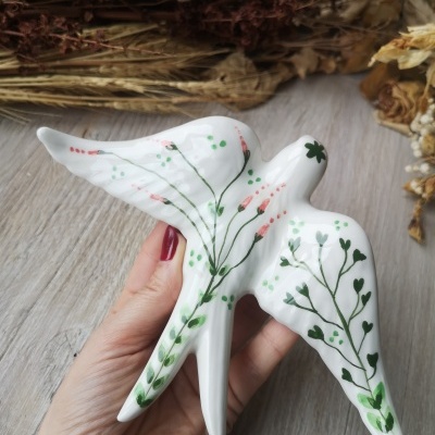 Pássaro decorativo branco com pintura floral segurado por mão com unhas vermelhas