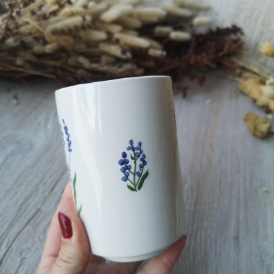 Caneca branca com flores azuis e folhas verdes