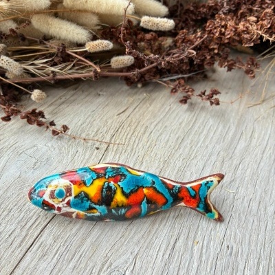 Figura decorativa em forma de peixe colorido sobre madeira com ramos secos ao fundo