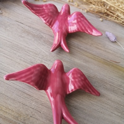 Esculturas de pássaros rosa em cerâmica brilhante sobre superfície de madeira com flores secas