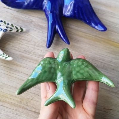 Objetos decorativos em forma de passarinho verde e azul sobre madeira clara