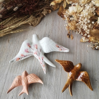 Três pássaros decorativos em cerâmica sobre madeira com ramos secos