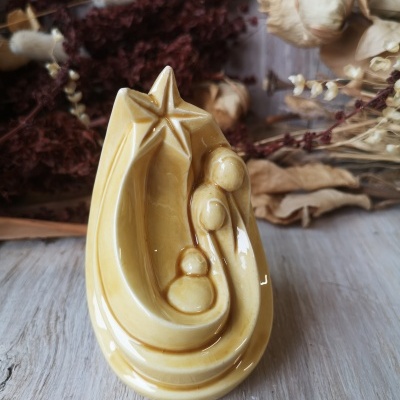 Figura de porcelana amarela representando a Sagrada Família sob uma estrela em fundo de flores secas