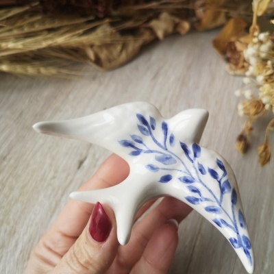 Peça decorativa em cerâmica branca em forma de pássaro com pintura azul de folhas