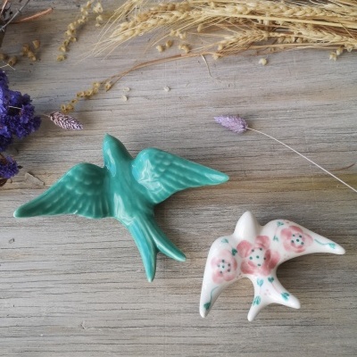 Dois passarinhos decorativos em cerâmica sobre madeira clara com flores secas.