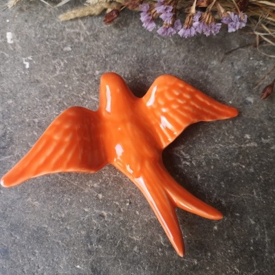 Figura decorativa laranja de pássaro em cerâmica sobre superfície cinzenta com flores secas