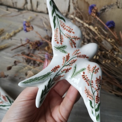 Pomba decorativa em cerâmica branca com flores pintadas segura por mão