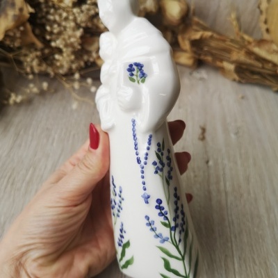 Estatueta branca de porcelana com flores azuis e verdes, figura humana segurando criança