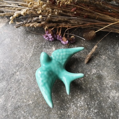 Estatueta de pássaro em cerâmica verde com flores secas ao fundo