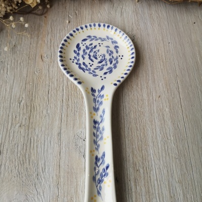 Colher de pau cerâmica branca com padrão azul e amarelo sobre madeira clara.