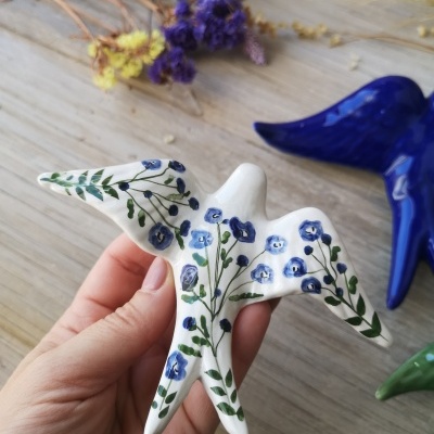 Pássaro em cerâmica pintado com flores azuis e folhas verdes