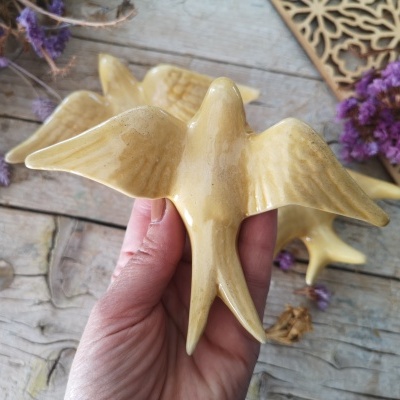 Pássaro amarelo em cerâmica com asas abertas na mão sobre fundo de madeira