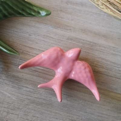 Pássaro decorativo rosa em cerâmica com textura sobre madeira clara