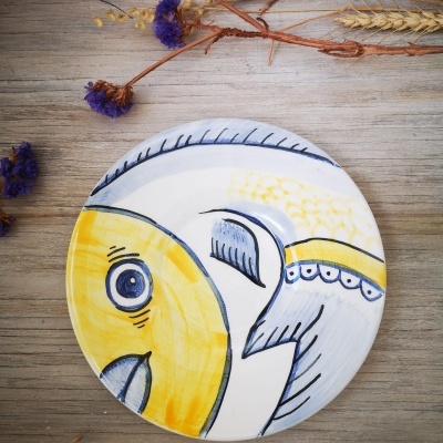 Prato decorativo de cerâmica com desenho de peixe em amarelo e azul sobre mesa de madeira