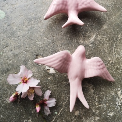 Dois pássaros decorativos rosa em cerâmica e flores cor-de-rosa num fundo cinzento