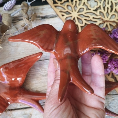 Pássaros de cerâmica castanhos brilhantes em mão sobre fundo rústico com flores e madeira