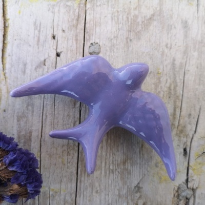 Escultura de pássaro lilás em cerâmica sobre madeira com flores secas ao lado