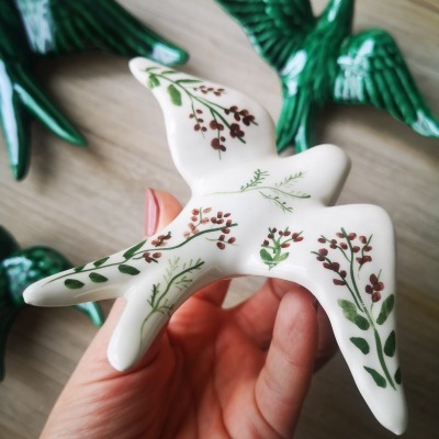 Figura decorativa em cerâmica branca com estampas florais segurada à mão