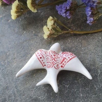 Estatueta branca em forma de ave com padrão vermelho e flores secas ao fundo