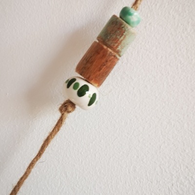 Corda castanha com contas de cerâmica e madeira pendurada em fundo branco