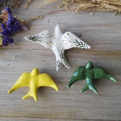 Três pássaros decorativos em cerâmica de várias cores sobre madeira com flores secas