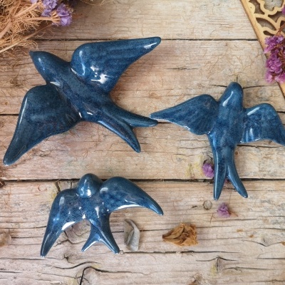 Três esculturas azuis de pássaros em cerâmica sobre madeira com flores secas