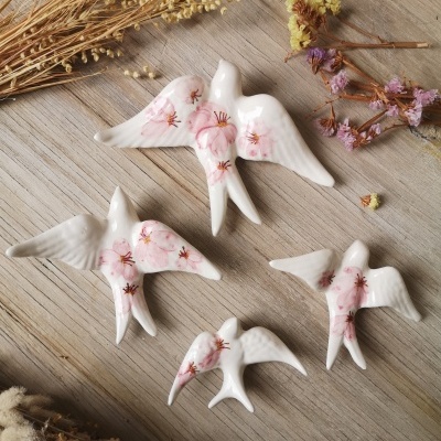 Quatro pássaros de cerâmica branca com pintura floral rosa sobre madeira com flores secas