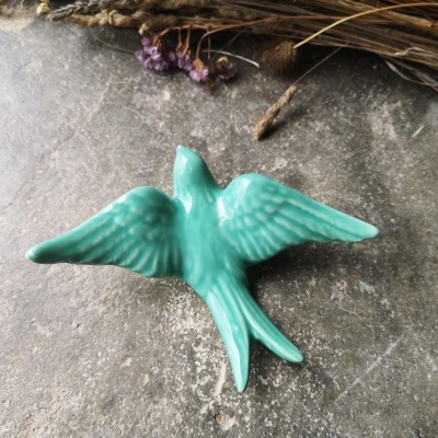 Figura em cerâmica verde de pássaro com asas abertas sobre pedra cinzenta