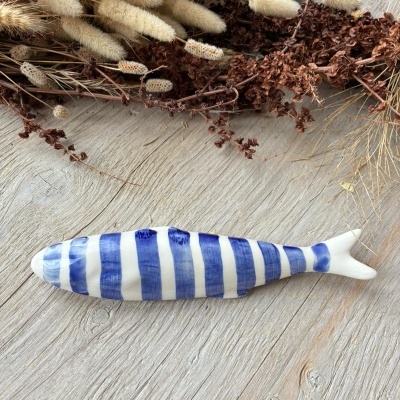 Peixe decorativo cerâmico azul e branco sobre madeira com ramos secos