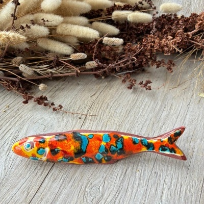 Peixe decorativo em cerâmica colorida sobre mesa de madeira clara com ramos secos.